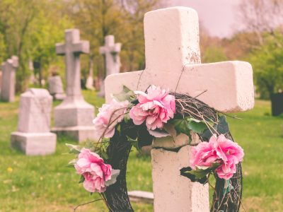 Funeral wreath with pink flower on a cross, in a cemetary, with a vintage filter.